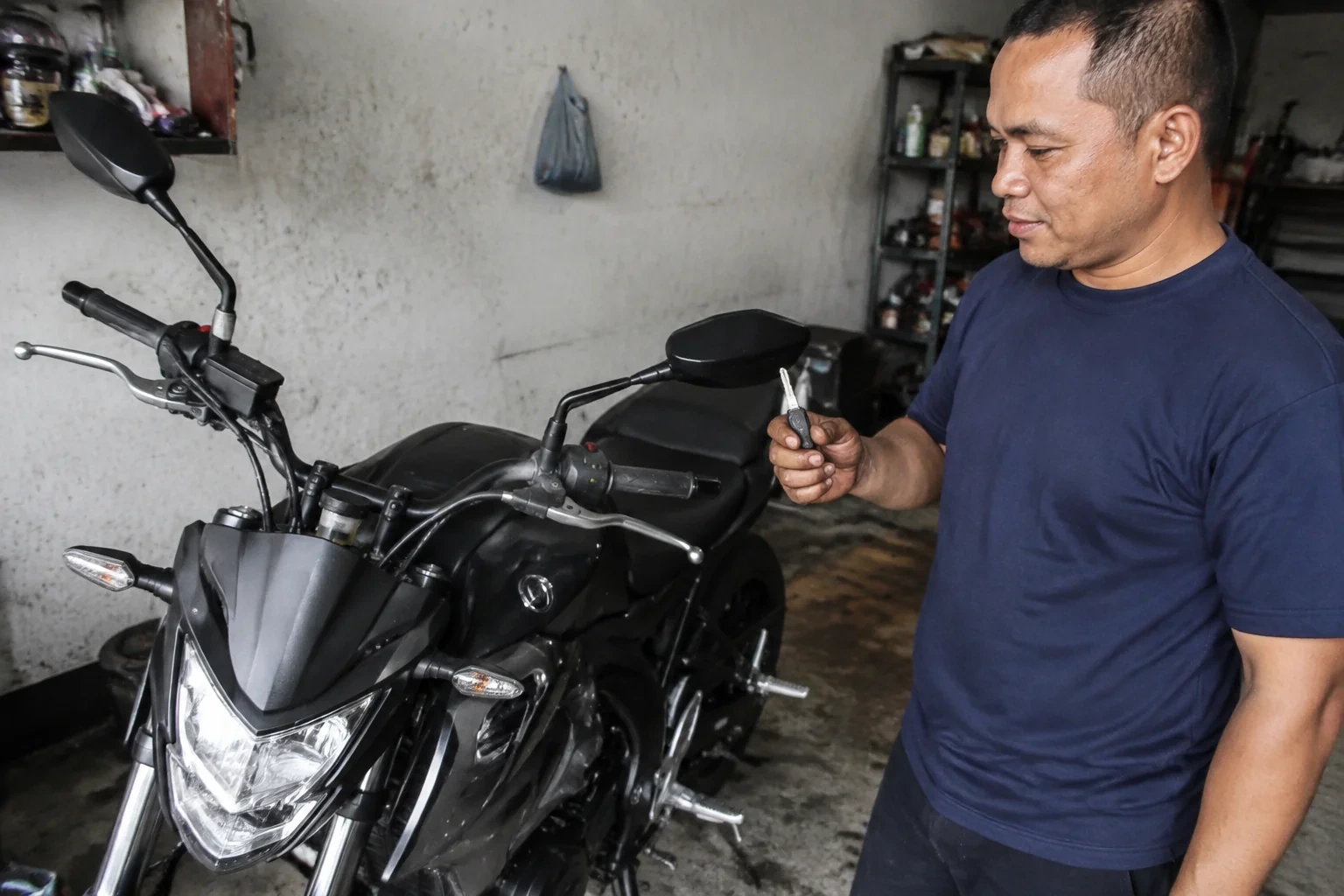 Person holding a key beside a black motorcycle in a garage.